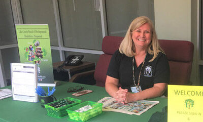 Smiling Employee From Human Resources Department Sitting At A Table Greeting Applicants During A Lake County Board Of DD At A Job Fair.