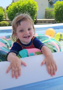 Photo of Grayson smiling and happy in a pool. Grayson receives services for Early Intervention.
